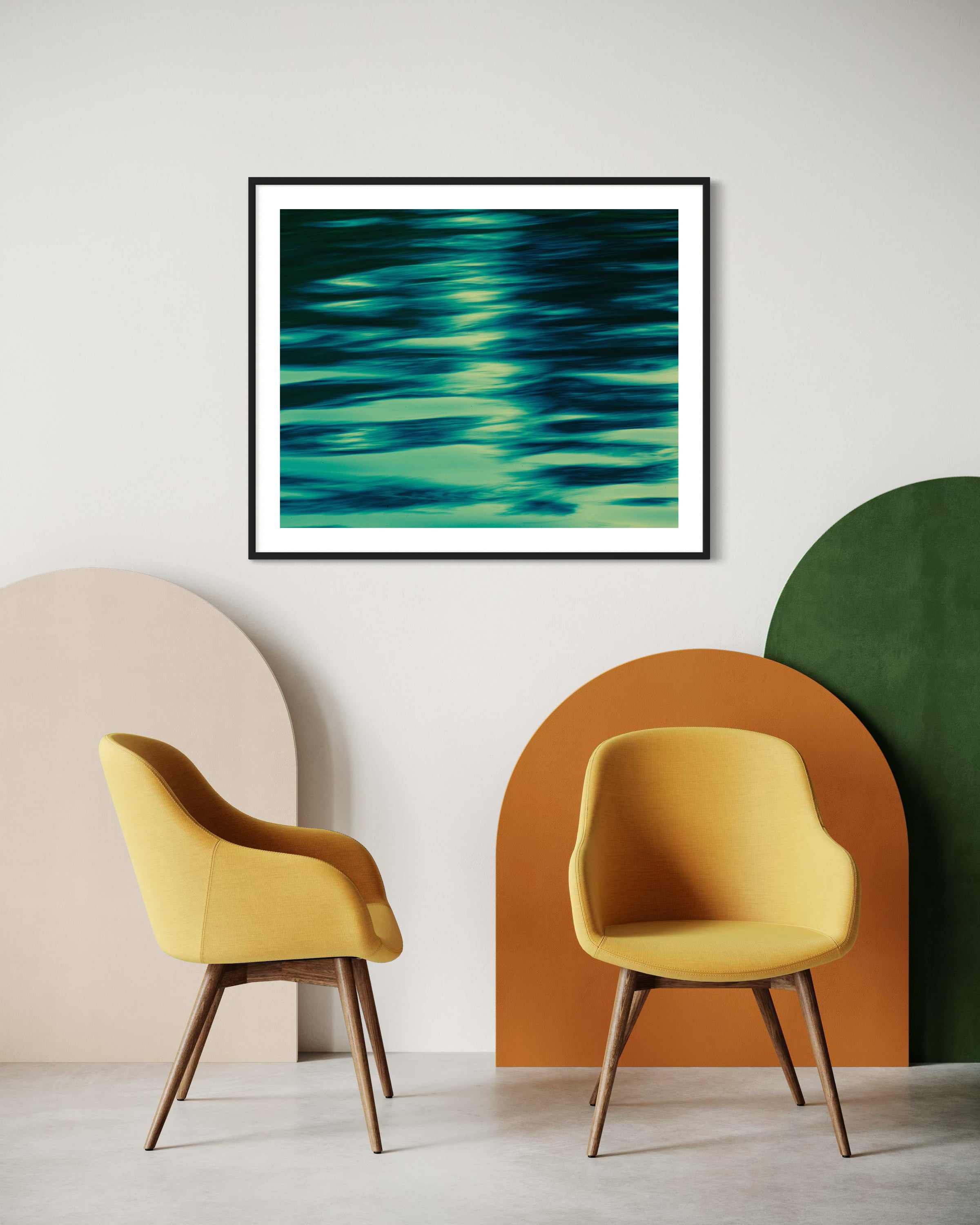 photo of abstract water in lake with blue, green and black in black frame with white matte on wall in modern minimalist sitting area with two yellow chairs and concrete floors