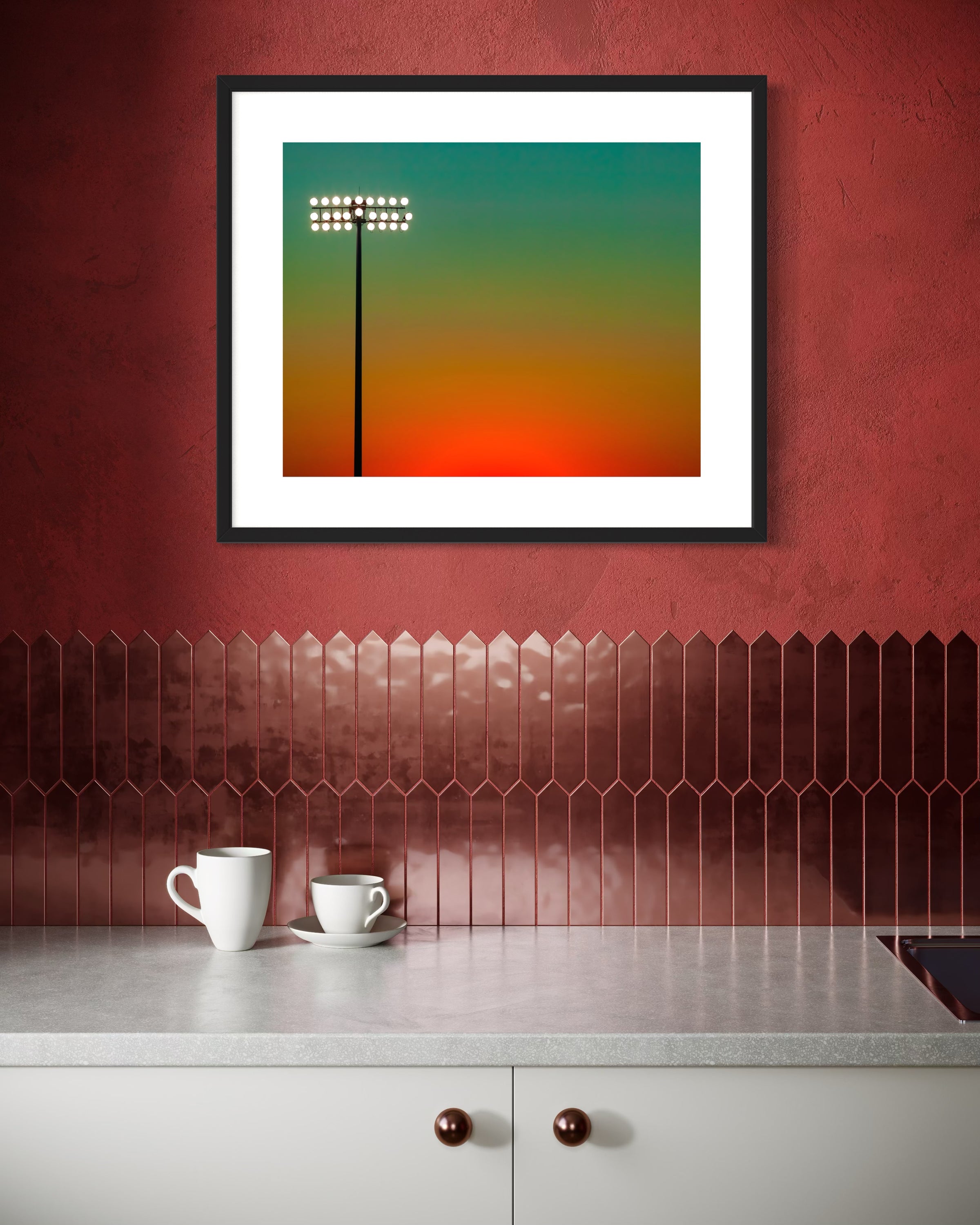 Framed abstract art piece on a red wall above a kitchen counter with two white cups.