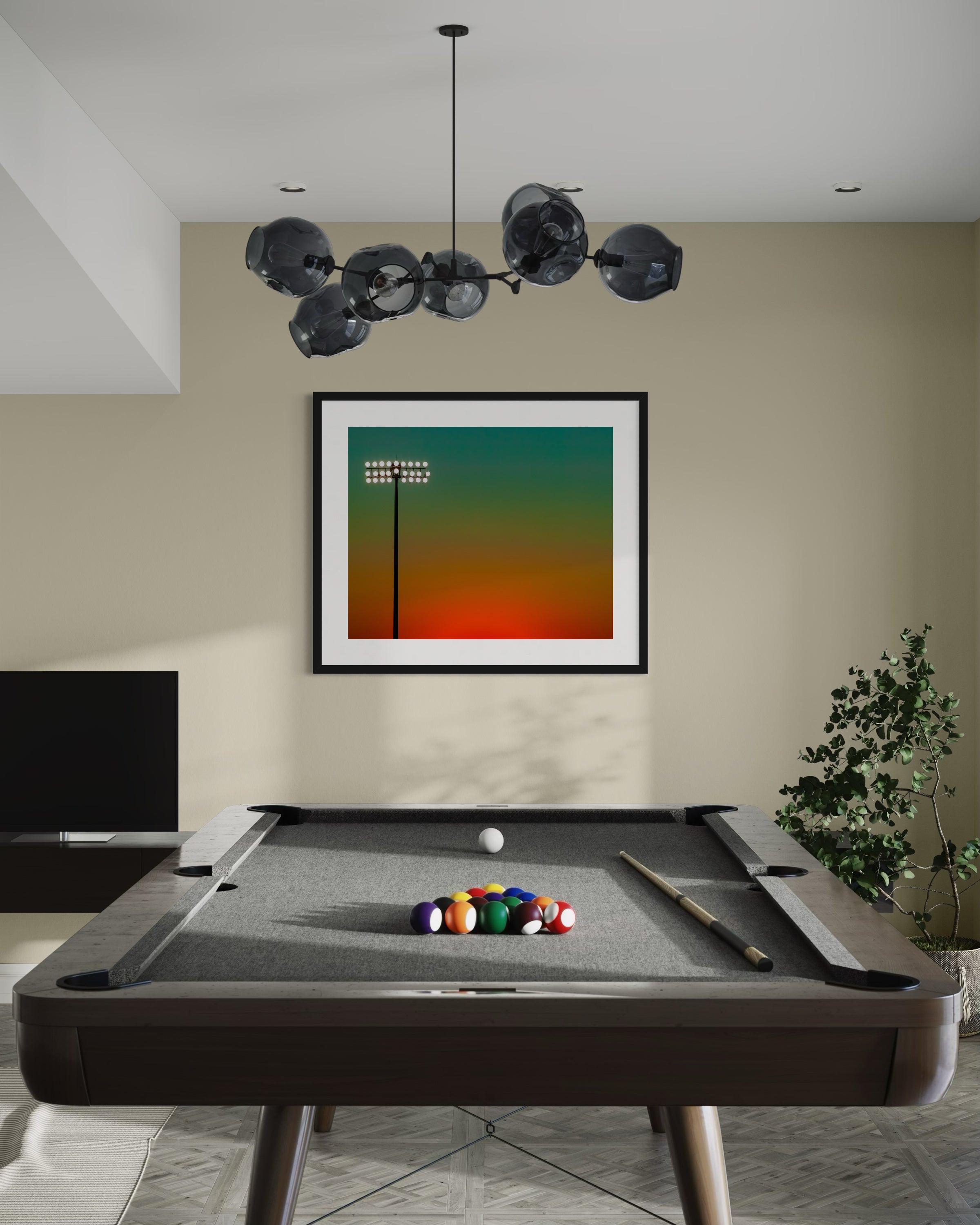 photo of sunset at football stadium single pole of lights left of center, gradient sky teal blue to pale yellow to orange gradient top to bottom in black frame with white matte on light tan wall in game room with pool table