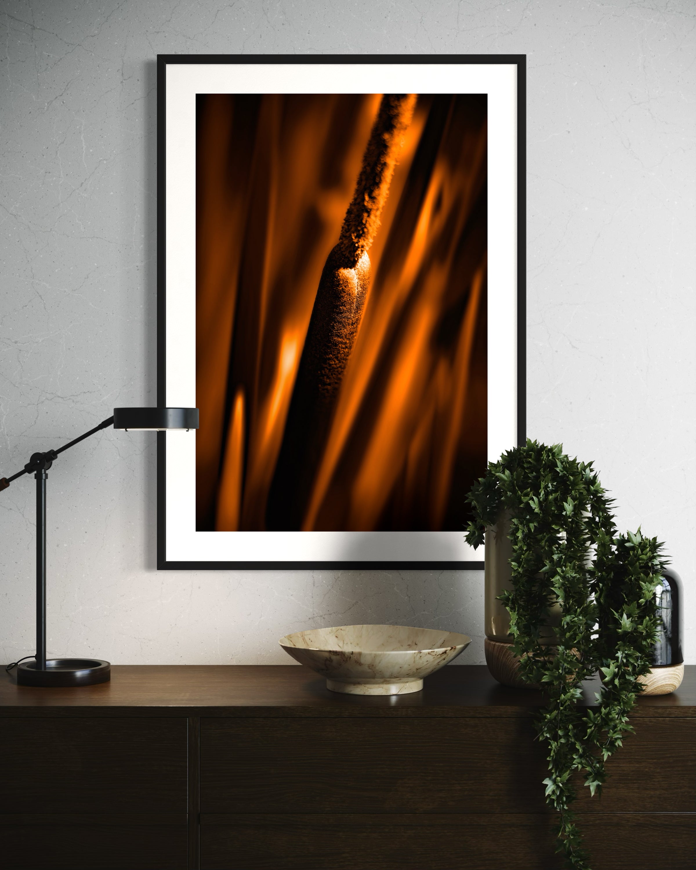 reeds in gold tone with selective focus photo in black frame on tan wall above small dark wooden table with drawers