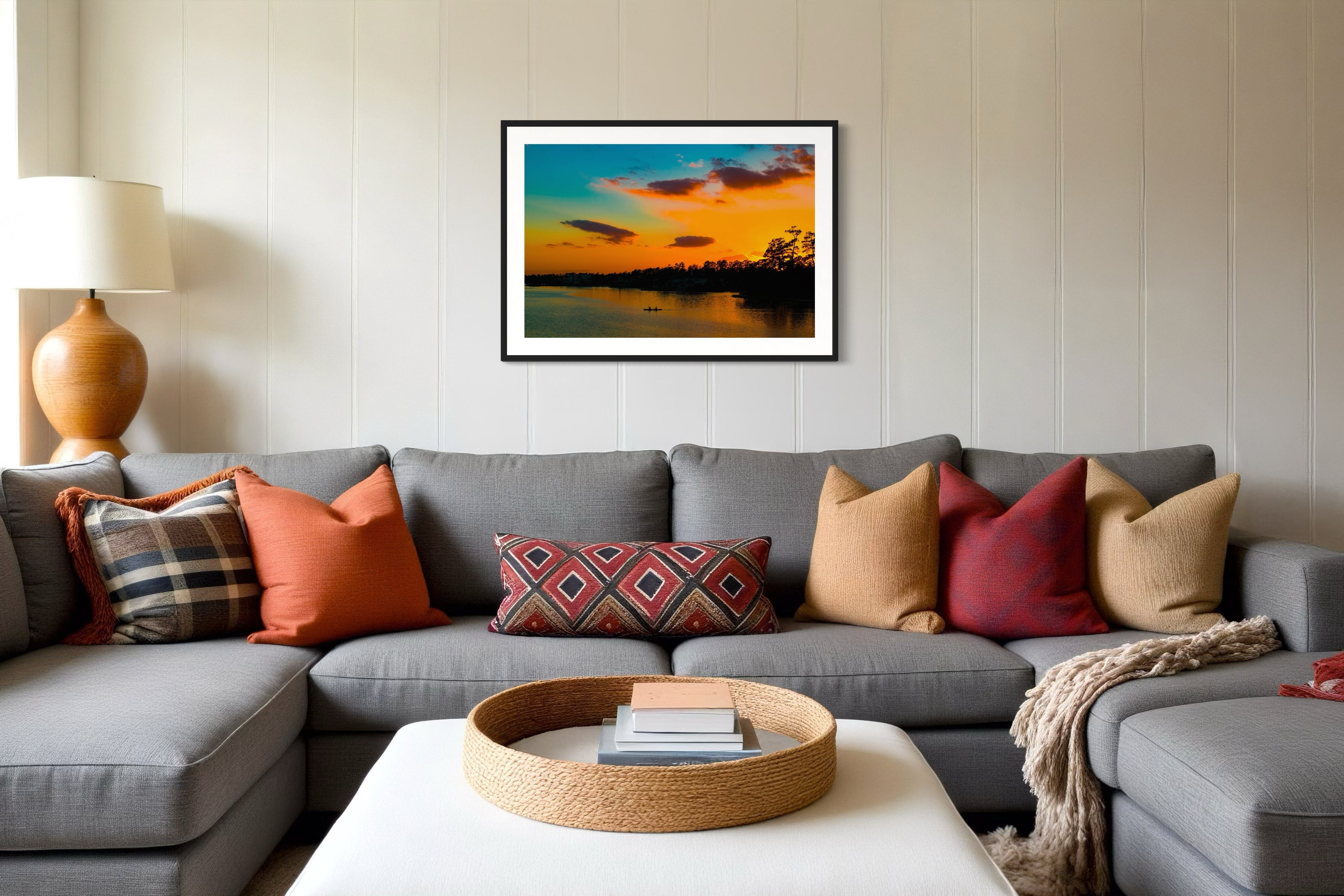 wide angle photo of kayak on lake at sunset in black frame with white matte on off white wall above gray couch in living room