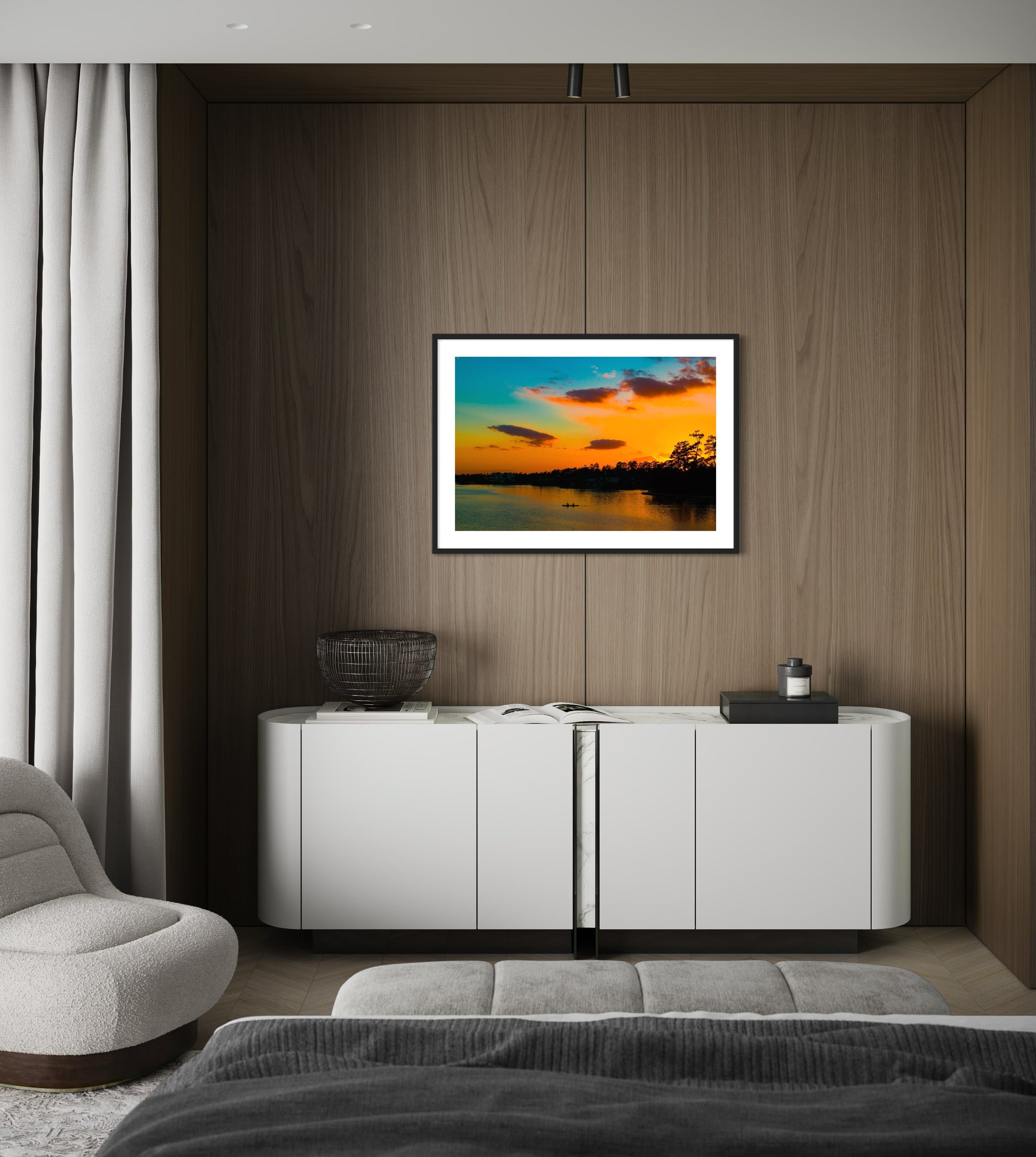 wide angle photo of kayak on lake at sunset in black frame with white matte on wooden wall above piece of modern furniture in modern bedroom