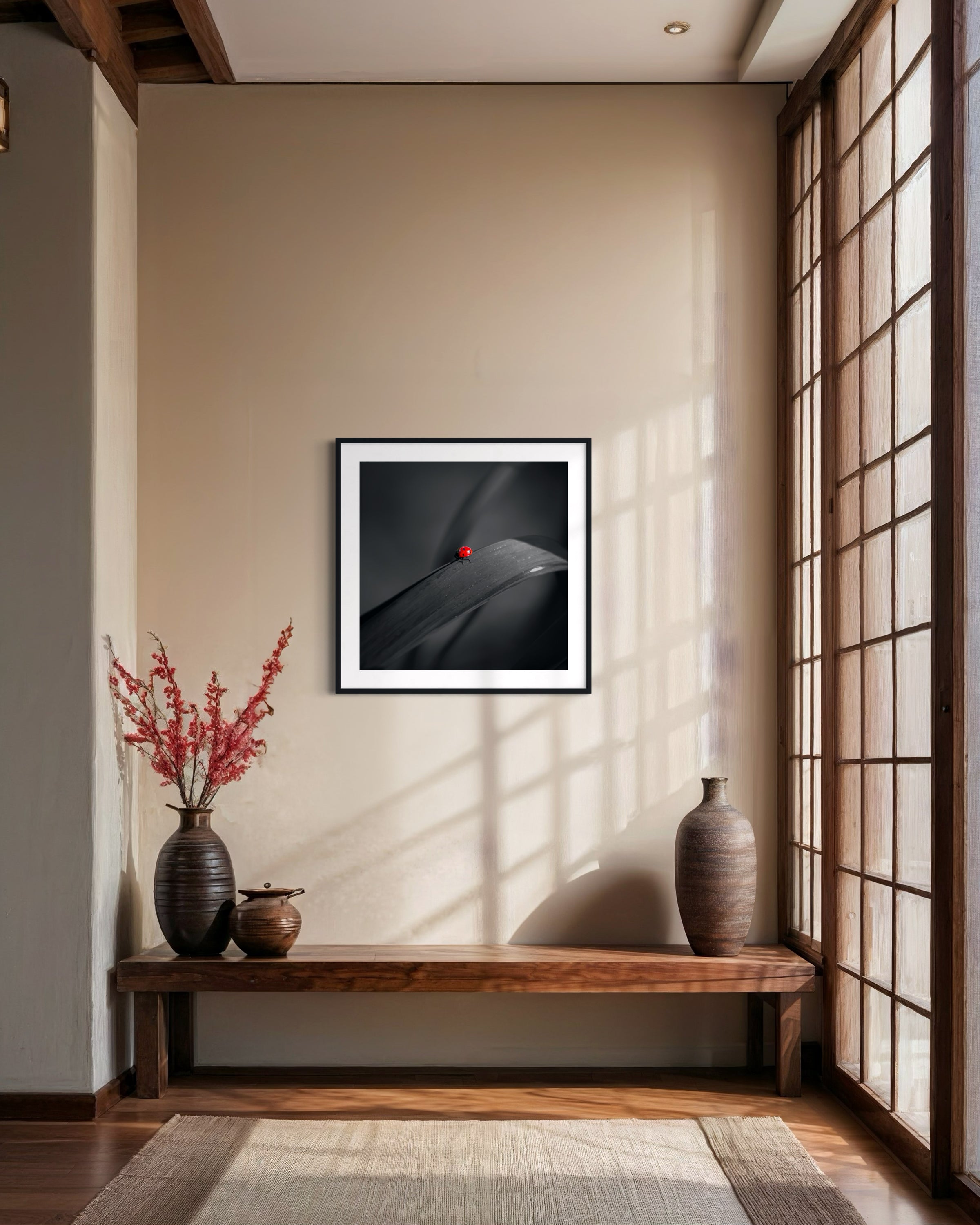 photo of Ladybug in middle of square image, everything except the Ladybug is black and white in black frame on tan wall with thick wooden bench below and floor to ceiling window on the right