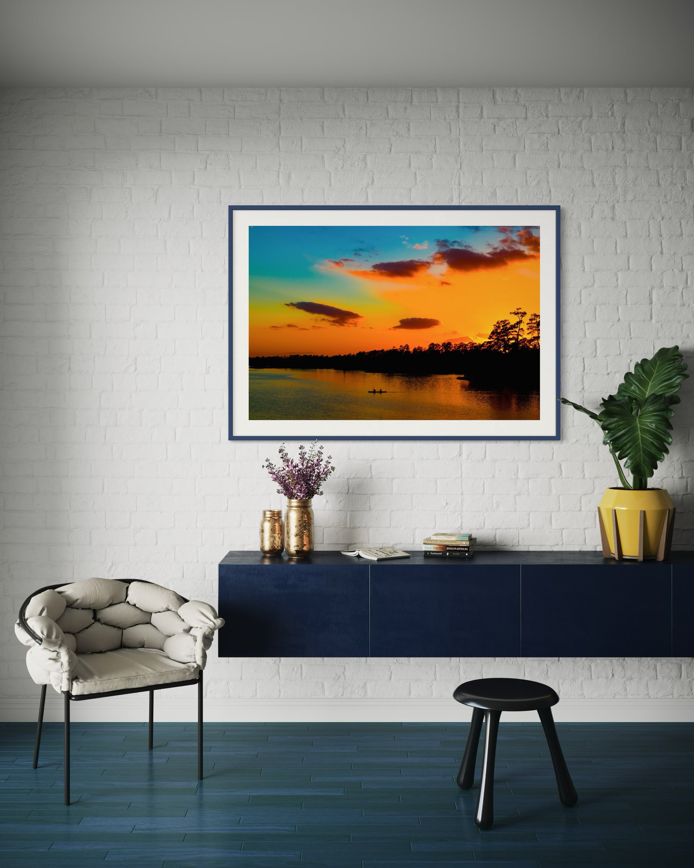 wide angle photo of kayak on lake at sunset in dark blue frame with off white matte on white brick wall in modern sitting area