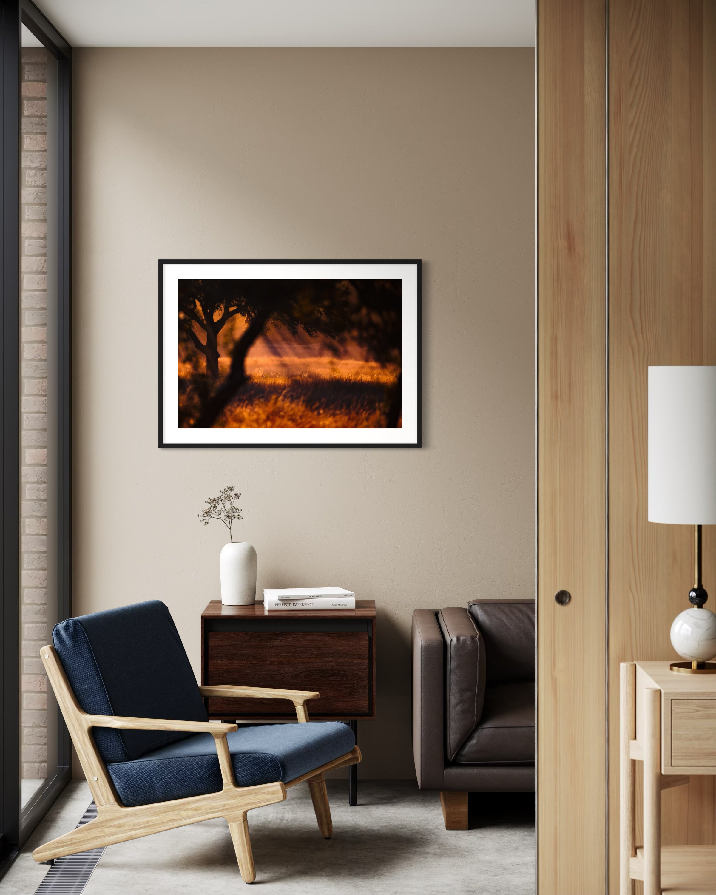 photo of rays of sunlight through the trees in black frame with white matte on tan wall in modern office with brown leather couch and blue chair