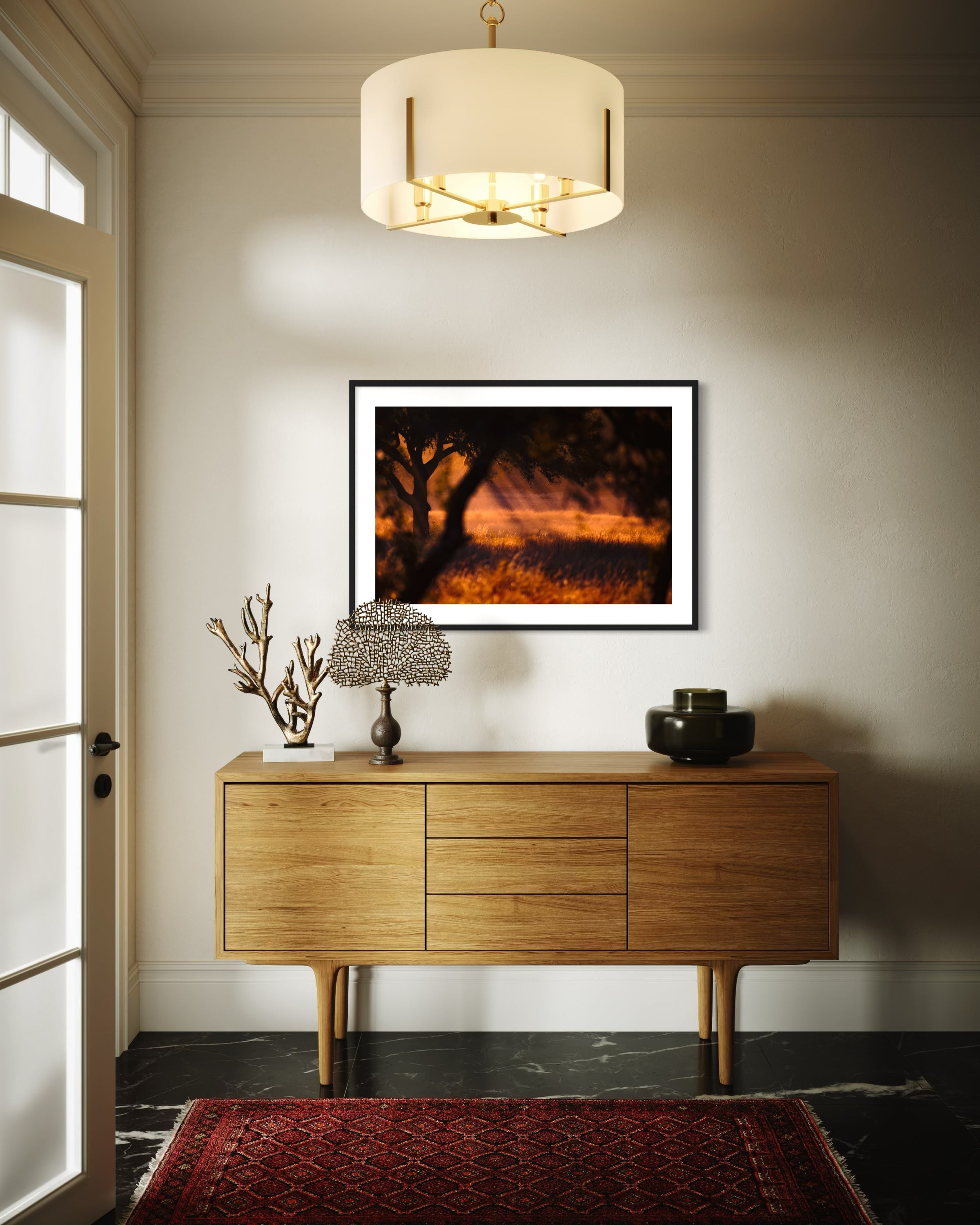 photo of rays of sunlight through the trees in black frame with white matte on tan wall above wooden piece of furniture with drawers in modern residential entry way with black marble floors