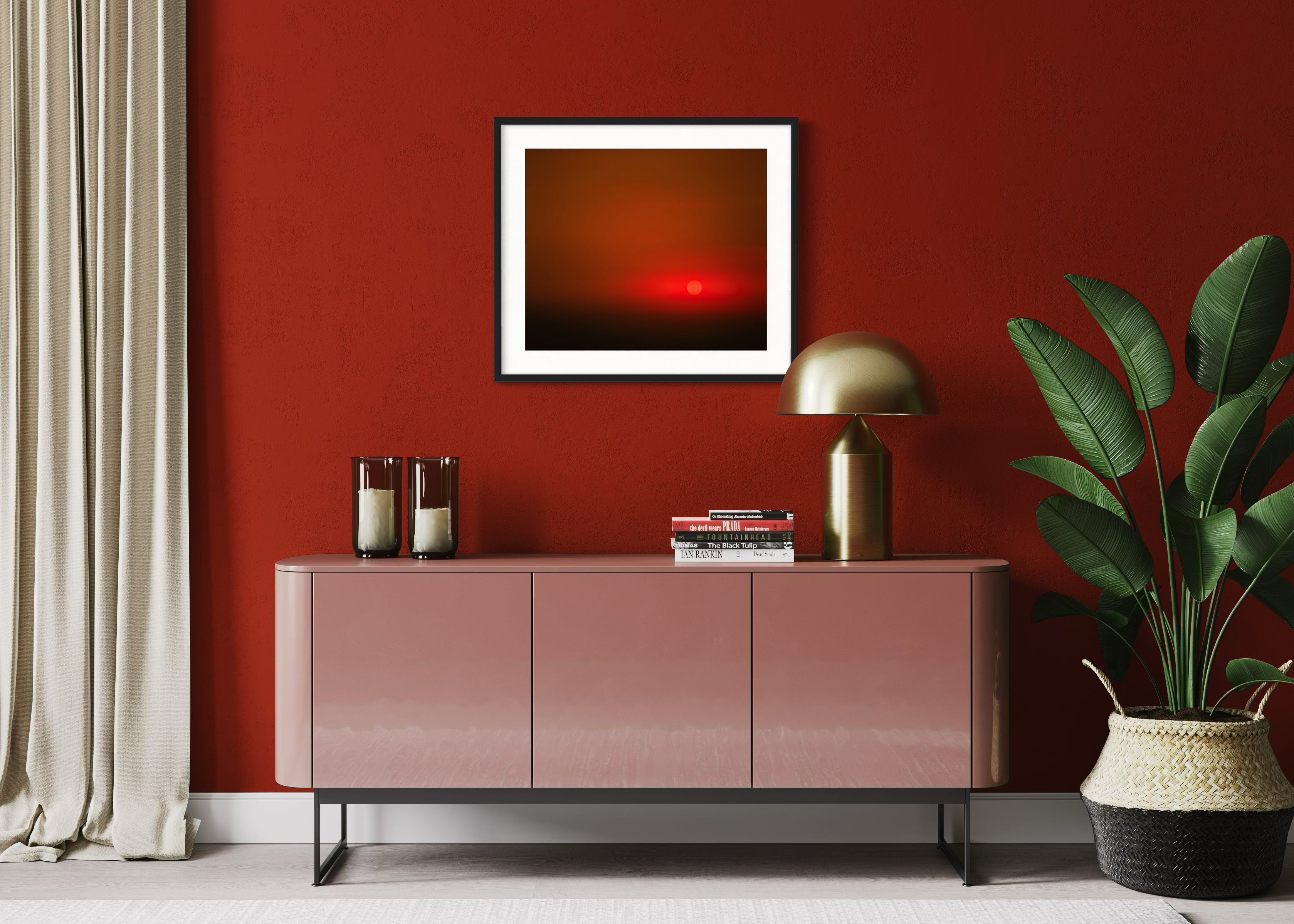 Modern living room with red walls, featuring a glossy pink sideboard, potted plant, gold lamp, beige curtains, and a framed abstract sunset art.