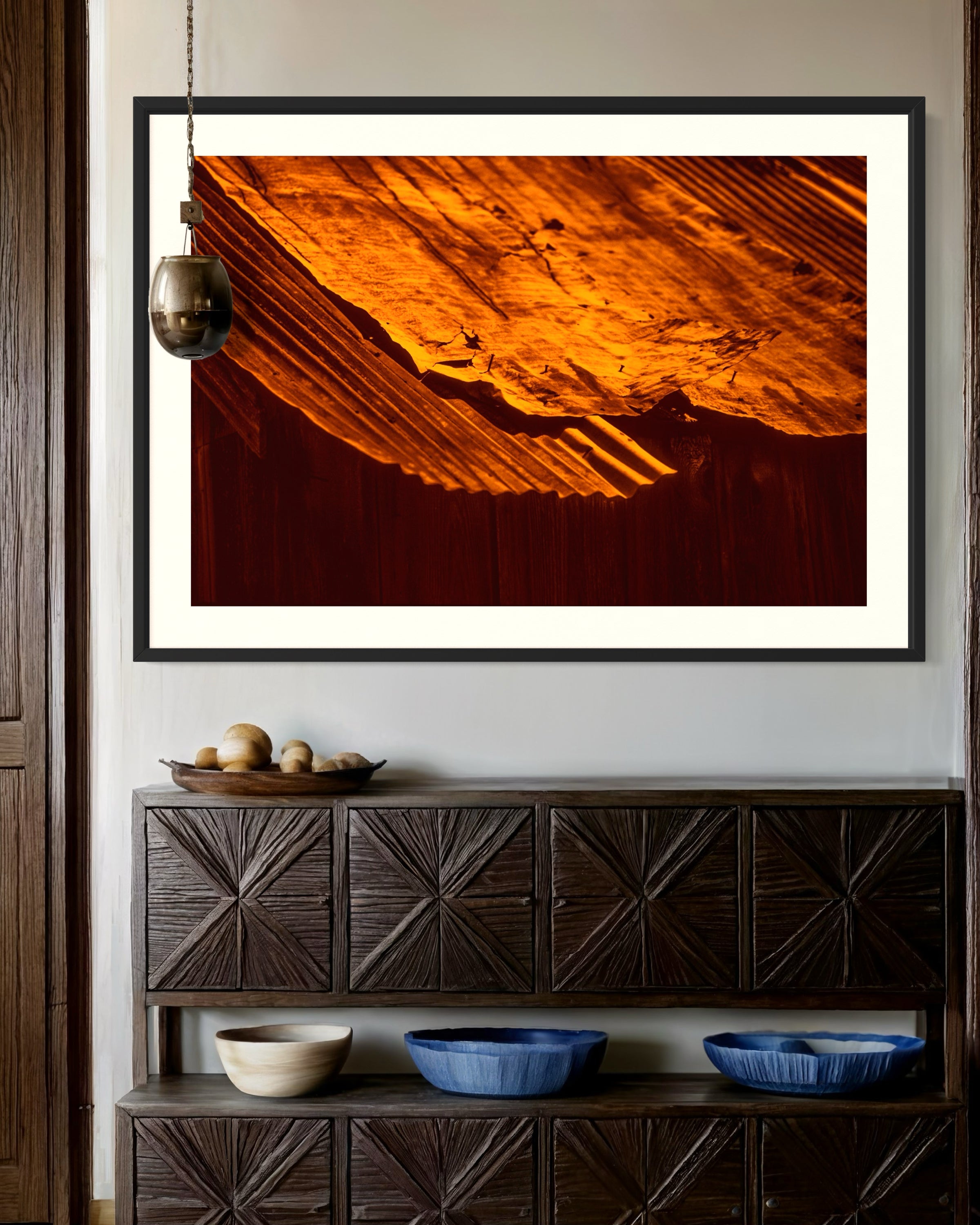 rusty old metal roof on old barn with warm tones photo in black frame on with off white matte on light tan wall above small wooden piece of furniture in rustic home