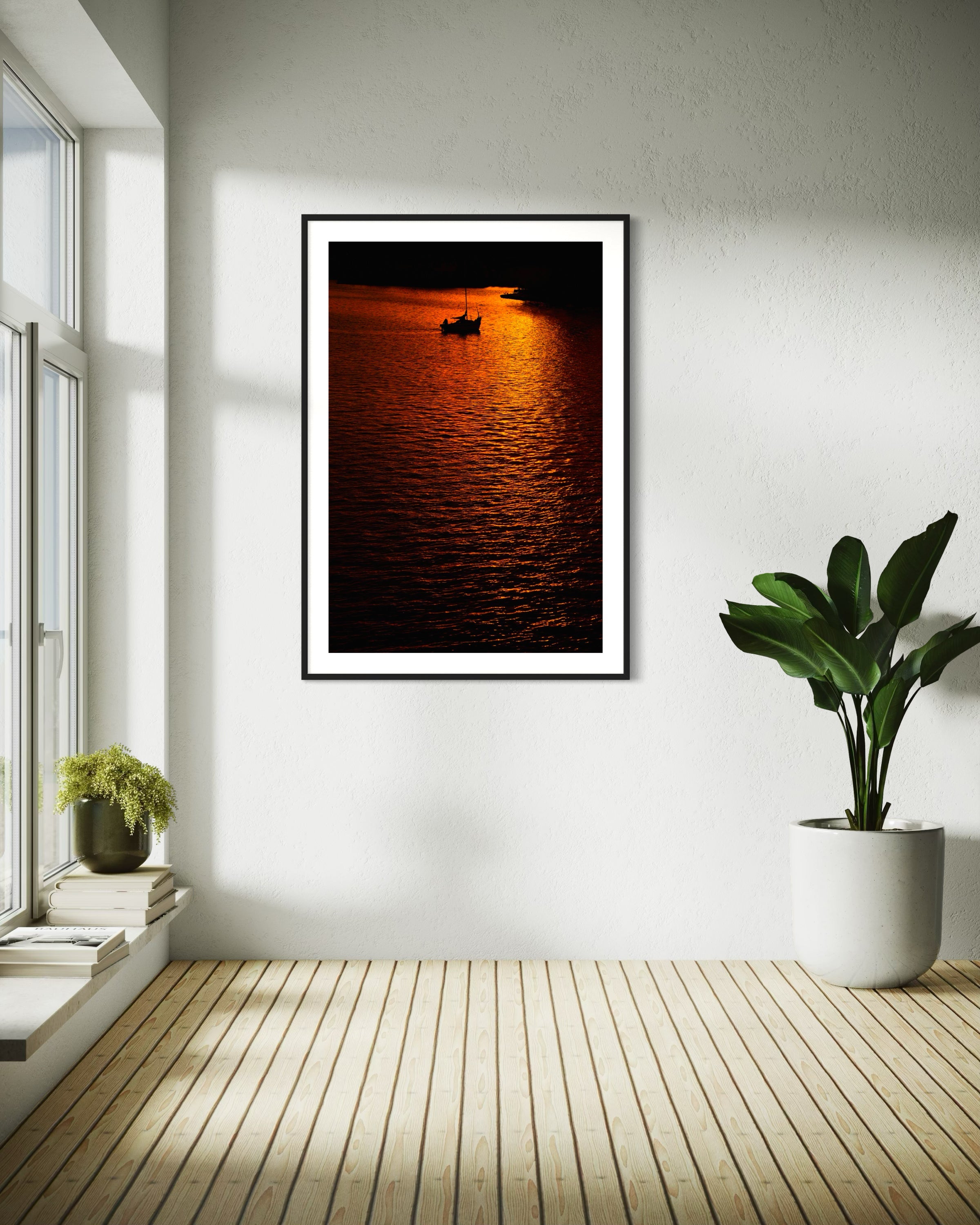 photo of sailboat sailing at sunset, in a very warm tone in black frame with white matte on white wall in corner of minimalist home
