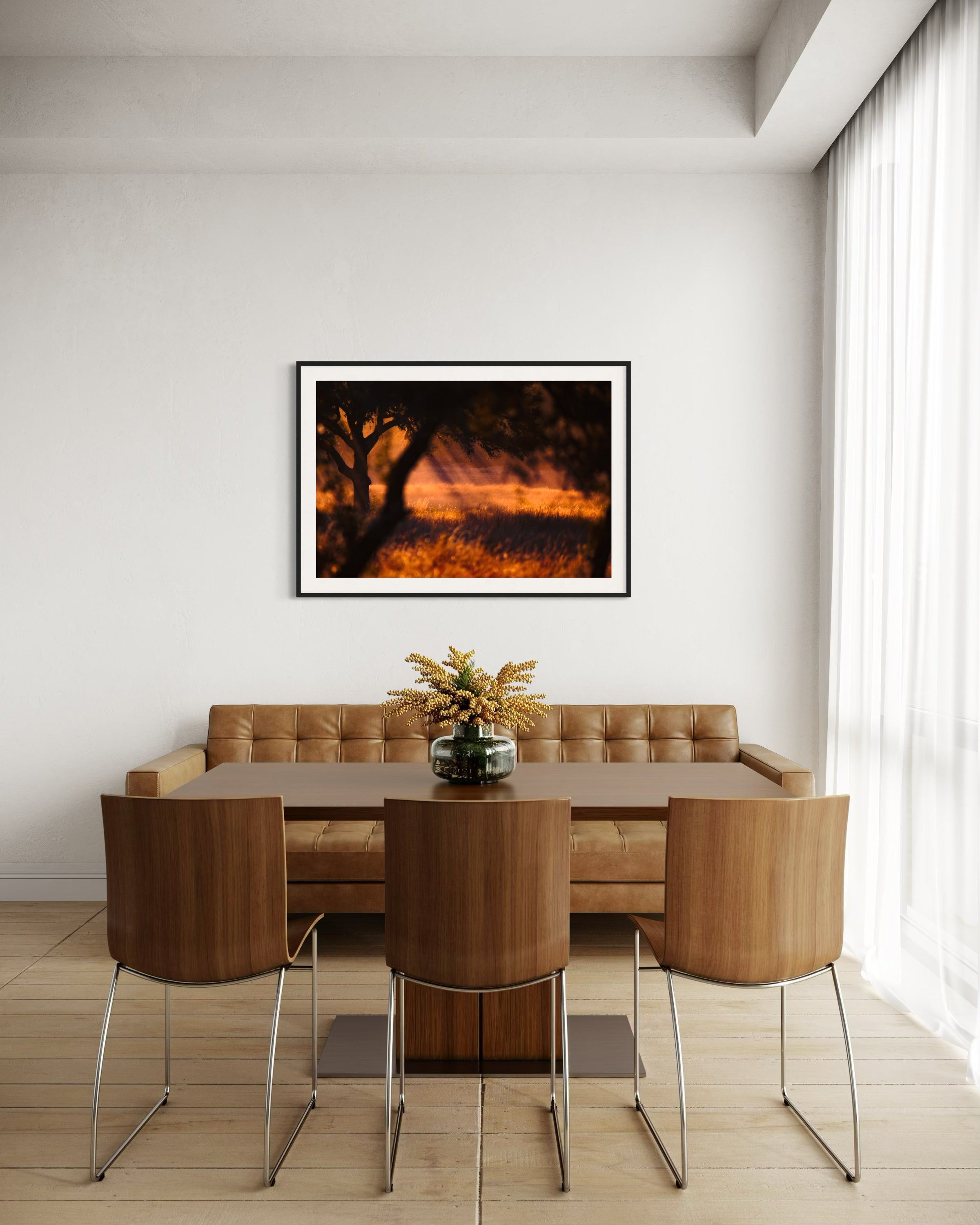 photo of rays of sunlight through the trees in black frame with off white matte on off white wall with soft window light and modern brown leather couch, wooden table and three wooden chairs