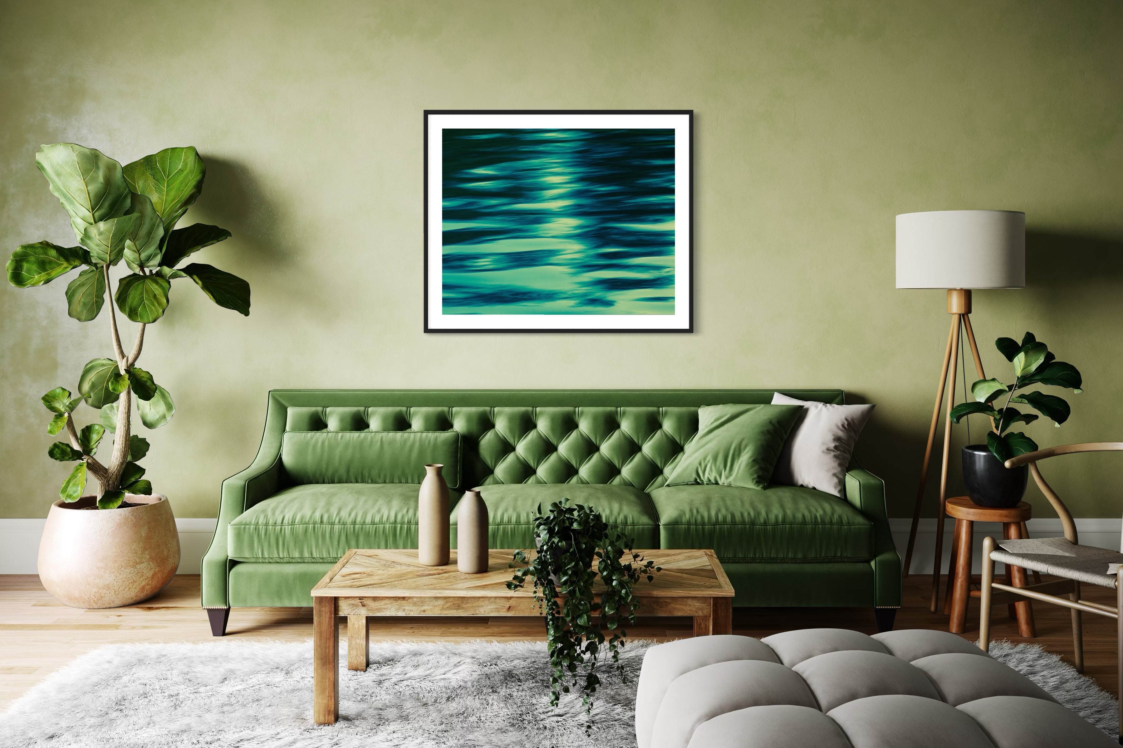 photo of abstract water in lake with blue, green and black in black frame on wall above couch in green toned room