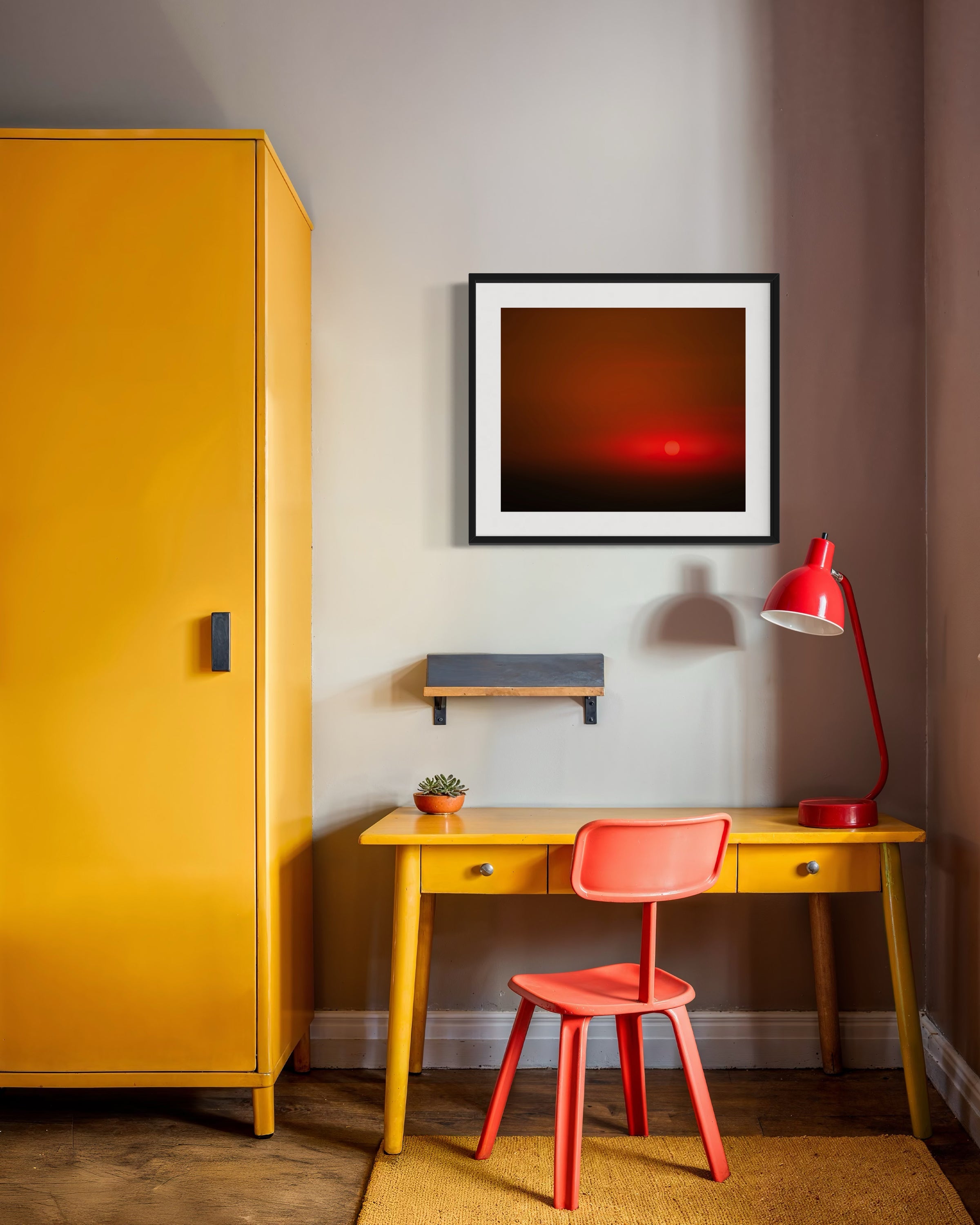 Yellow desk with red chair and lamp in a room with a yellow cabinet and framed artwork.