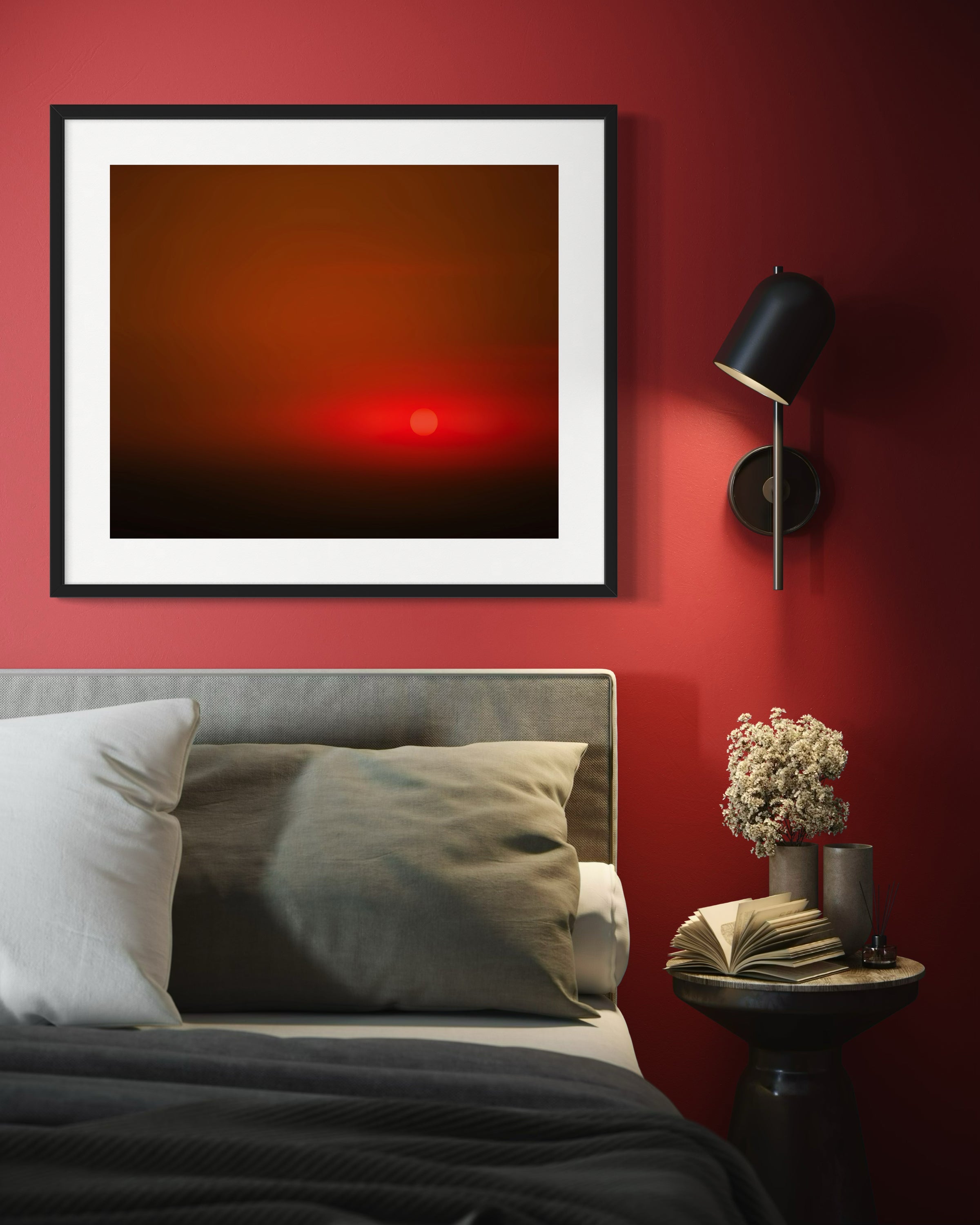 Framed abstract artwork on a red wall above a bed with a side table and lamp.