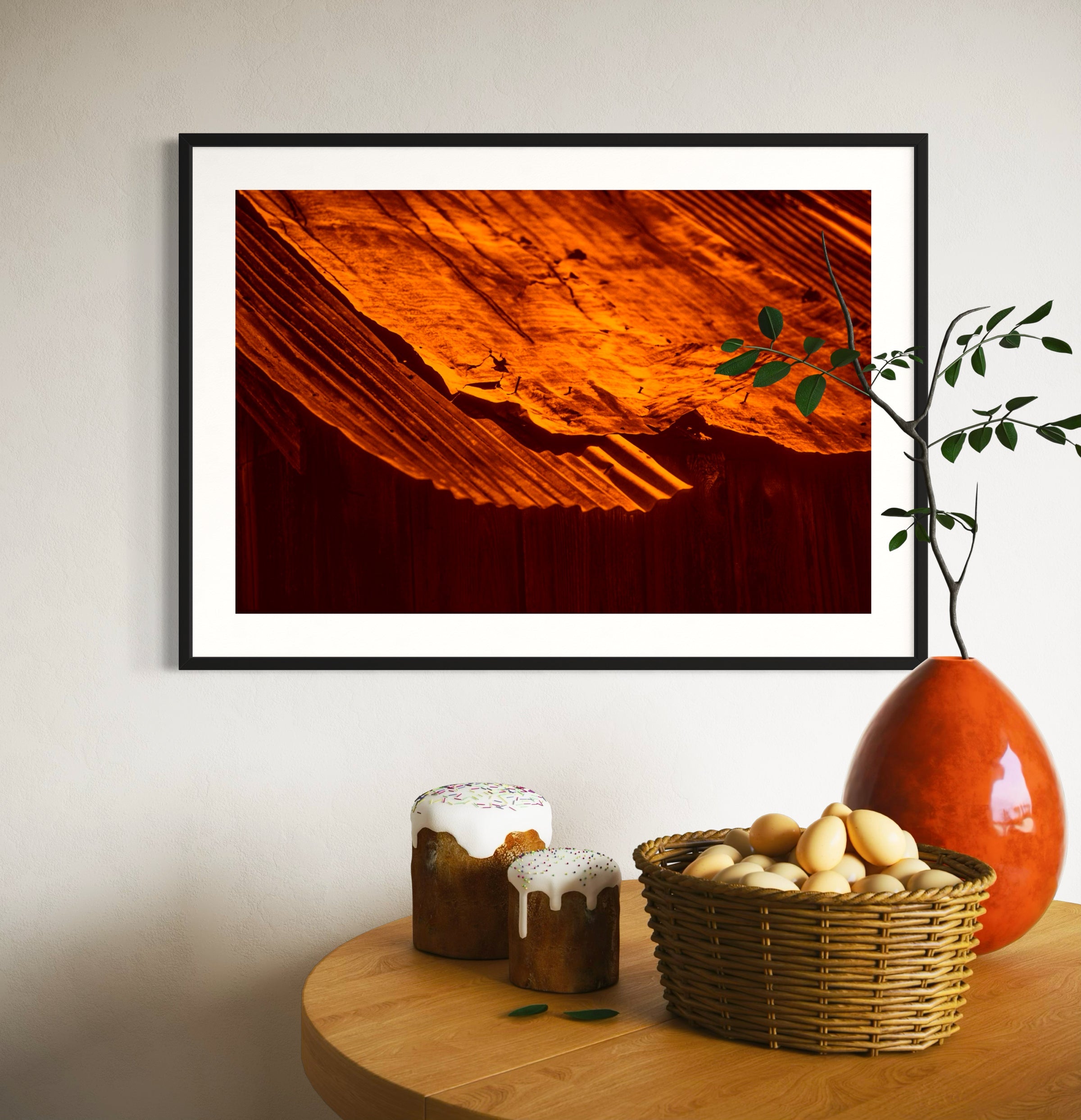 rusty old metal roof on old barn with warm tones photo in black frame with white matte on off white wall above small round table with basket of eggs and two small cakes